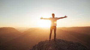 Smiling man on a mountain at sunrise with arms open, symbolizing freedom, motivation, and personal success