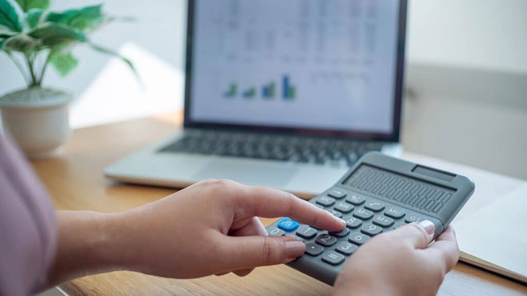 a person using a calculator on a desk in front of a laptop