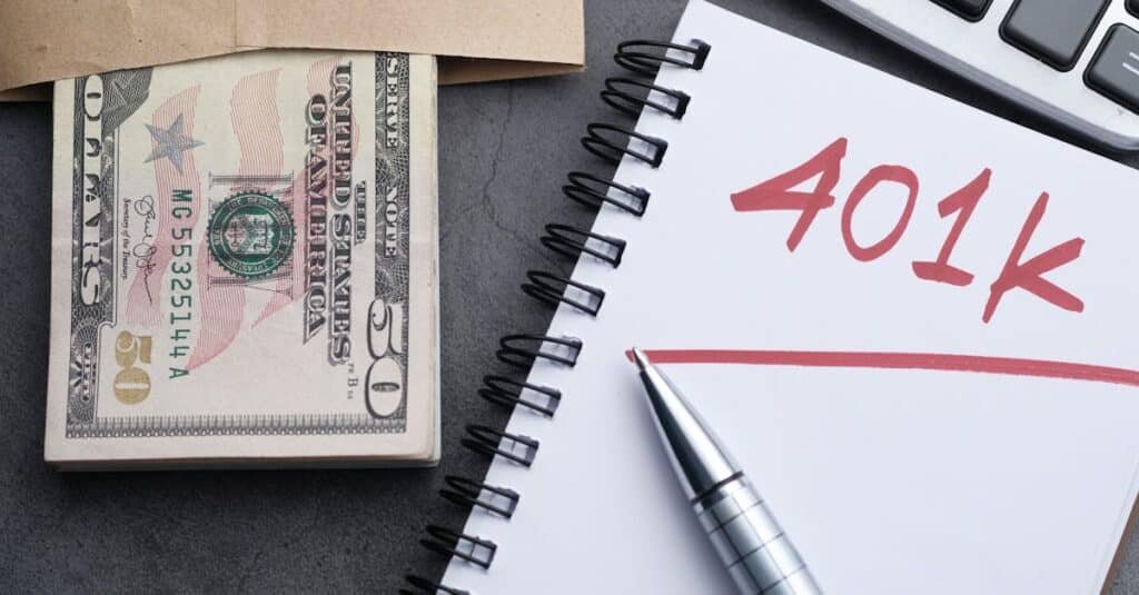 A desk setup with a notebook labeled '401k', a pen, cash, and a calculator representing financial planning.