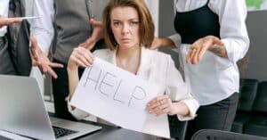 Stressed office worker holding a help sign surrounded by colleagues' demands.