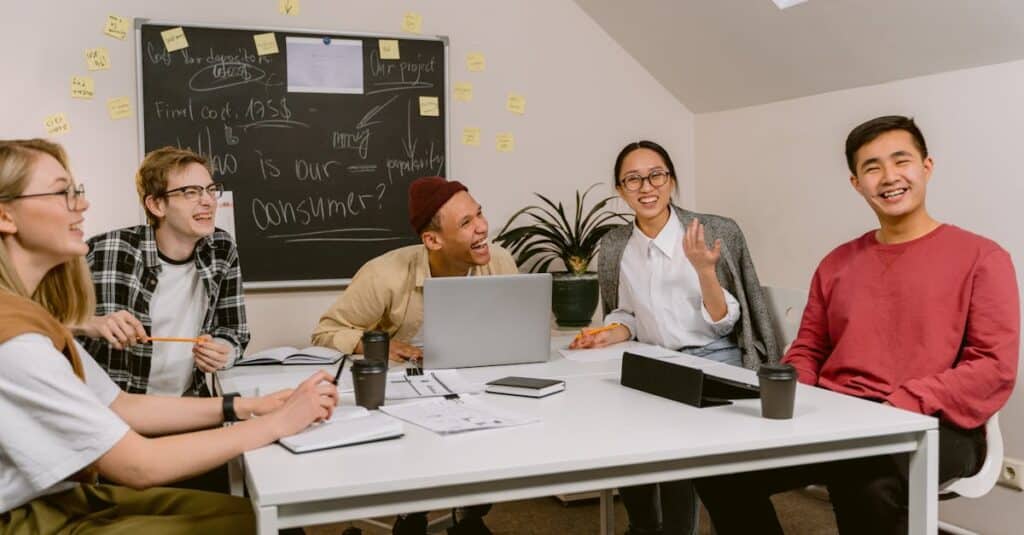 A diverse team of young professionals sharing ideas and laughing during a business meeting in a modern office setting.