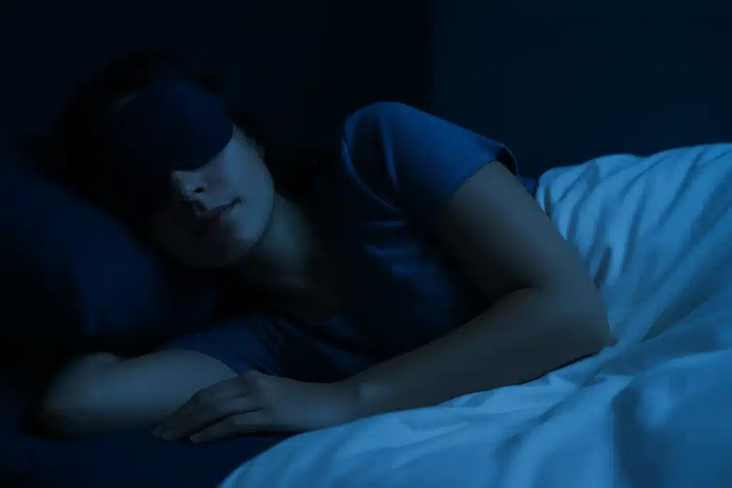 Woman sleepmaxxing with sleep mask in a dark, calm room