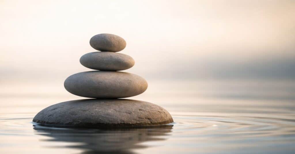 A balanced stack of smooth stones reflected in calm water, symbolizing stillness, focus, and composed leadership.