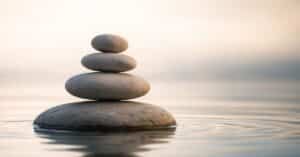 A balanced stack of smooth stones reflected in calm water, symbolizing stillness, focus, and composed leadership.