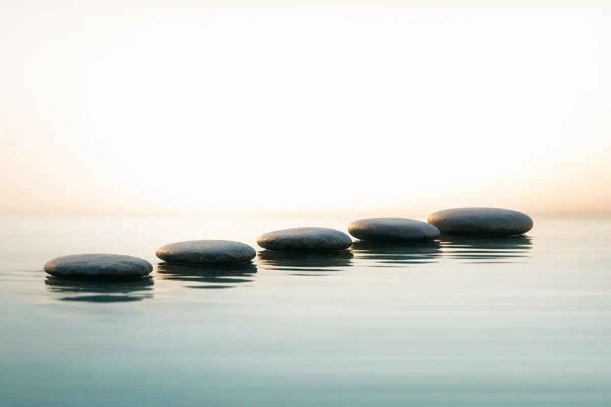 Five ascending stepping stones across calm water in soft morning light — a staged, deliberate career change in your 40s