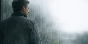 men in his forties standing quietly by a foggy window, thinking about which direction to point his next twenty years